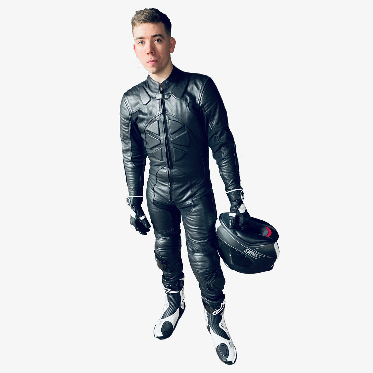 Man wearing a full-body black leather motorcycle racing suit holding a helmet on a white background - Front view